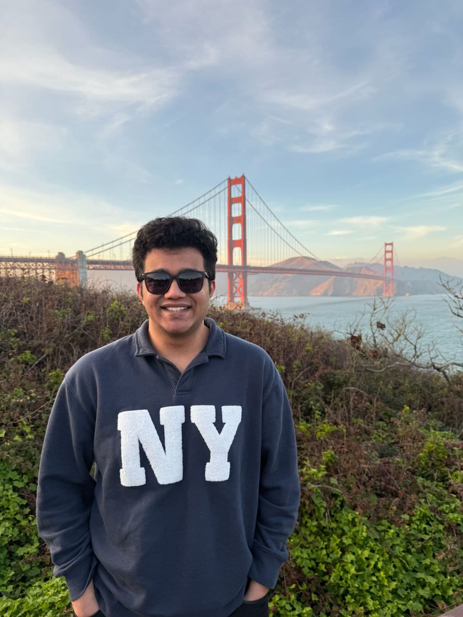 Pratyush in sunglasses and an NY sweatshirt in front of the Golden Gate Bridge